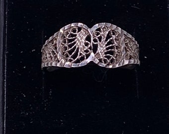 Puede incluir: Un anillo de filigrana de plata con un diseño delicado e intrincado. El anillo está hecho de dos círculos superpuestos con un patrón floral.