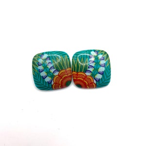 May include: A pair of square-shaped earrings with a floral design. The earrings are turquoise blue with orange, yellow, white, and green flowers.
