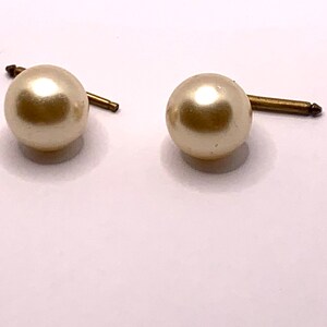 May include: A pair of pearl earrings with gold posts. The pearls are white and round.