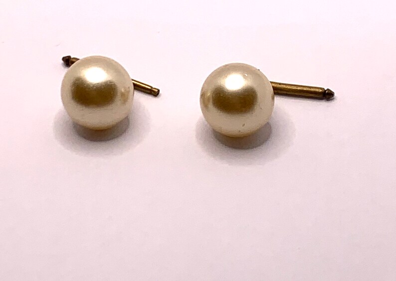 May include: A pair of pearl earrings with gold posts. The pearls are white and round.