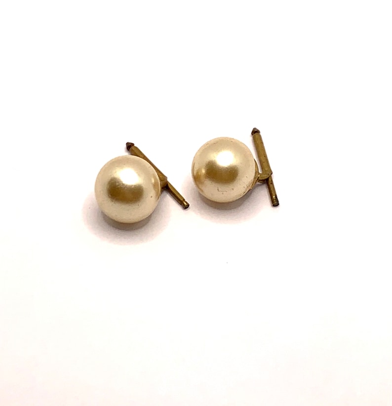 May include: A pair of pearl cufflinks with gold-toned metal accents. The pearls are round and white.