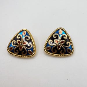 May include: A pair of triangular stud earrings. Each earring features a gold-tone frame with a blue, black, and red floral design. The earrings have a gold rope-like border and are set against a white background.