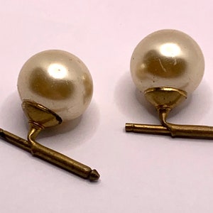 May include: A pair of gold cufflinks with a large, round, off-white pearl on each cufflink.