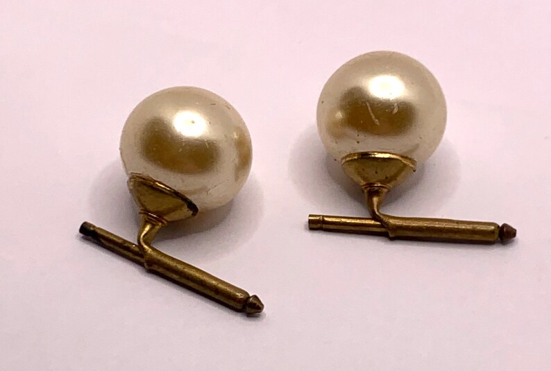 May include: A pair of gold cufflinks with a large, round, off-white pearl on each cufflink.