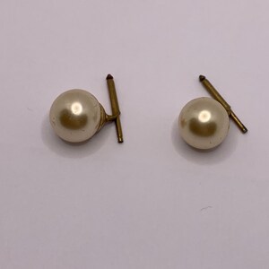 May include: A pair of gold tone pearl earrings with a simple design.