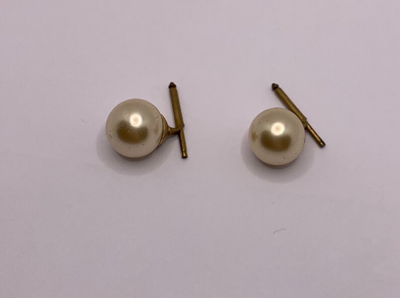 May include: A pair of gold tone pearl earrings with a simple design.