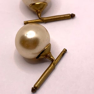 May include: A pair of gold cufflinks with faux pearl accents. The pearls are round and white.