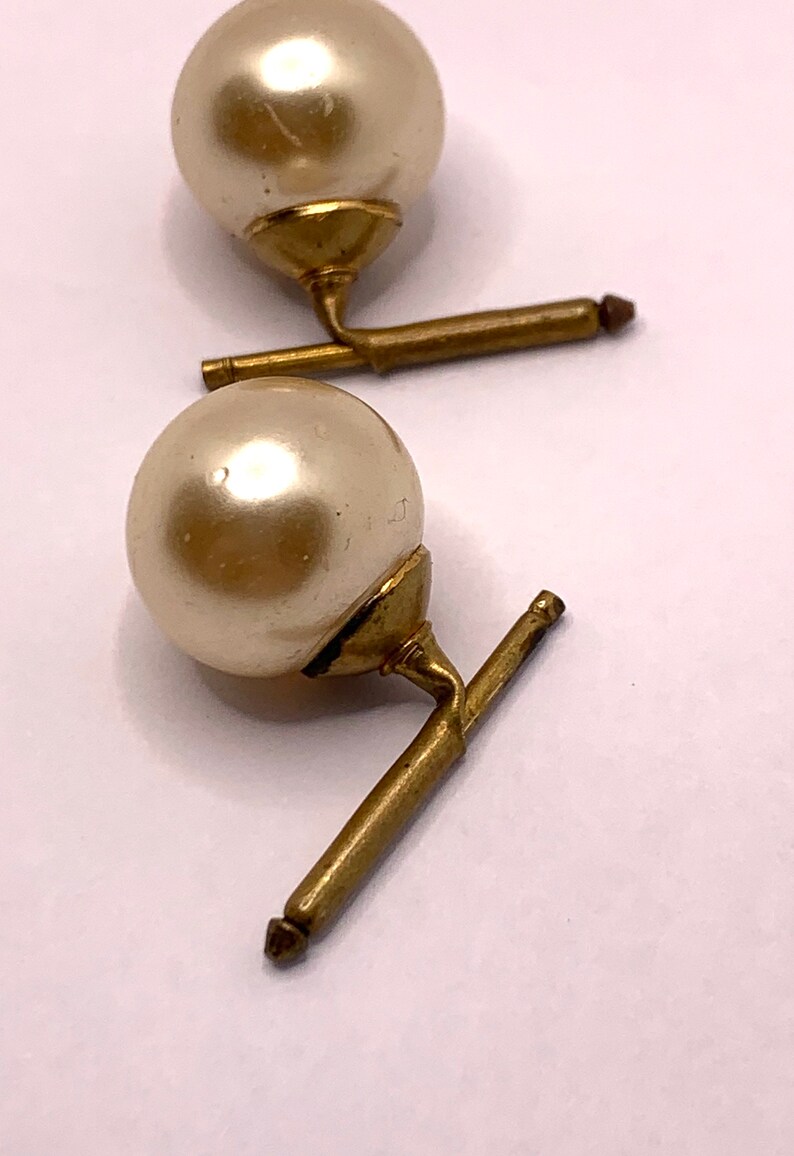 May include: A pair of gold cufflinks with faux pearl accents. The pearls are round and white.