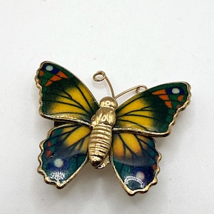 Puede incluir: Broche de mariposa dorada con detalles de esmalte amarillo, verde, azul y naranja. La mariposa tiene un cuerpo y antenas detallados, y las alas están extendidas. Un accesorio de estilo vintage.