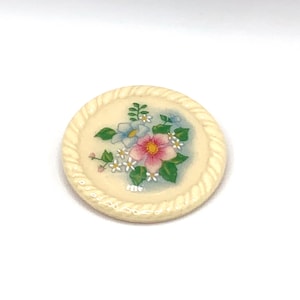 Broche vintage redondo de cerâmica creme com buquê floral de primavera.
