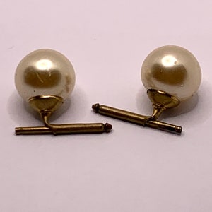 May include: A pair of cufflinks with a gold metal bar and a white pearl on each end.