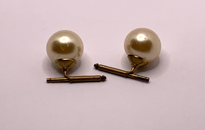 May include: A pair of cufflinks with a gold metal bar and a white pearl on each end.