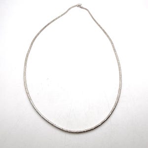 May include: A silver-toned snake chain necklace featuring a smooth, flexible design with a subtle metallic sheen. The necklace is circular in shape and includes a small, secure clasp mechanism at the top, showcasing a clean and polished appearance.