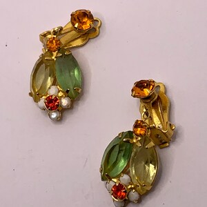 May include: A pair of gold-tone clip-on earrings featuring marquise-cut light green and yellow crystals, accented with small round orange and white stones. Each earring has a circular orange crystal at the top and a cluster of stones at the base.