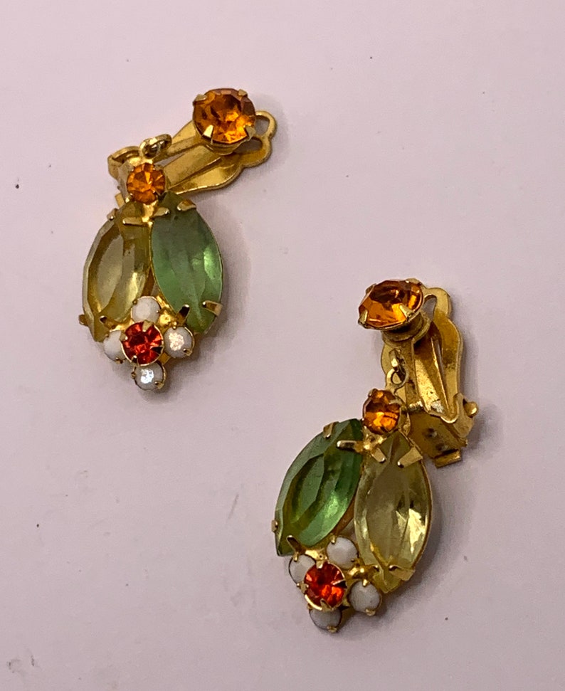 May include: A pair of gold-tone clip-on earrings featuring marquise-cut light green and yellow crystals, accented with small round orange and white stones. Each earring has a circular orange crystal at the top and a cluster of stones at the base.