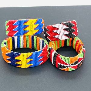 Puede incluir: Cuatro pulseras de cuentas de colores vibrantes. Las pulseras presentan intrincados patrones en rojo, azul, amarillo, verde, naranja, negro y blanco. Los diseños parecen geométricos e inspirados en tribus, mostrando una variedad de formas y combinaciones de colores.