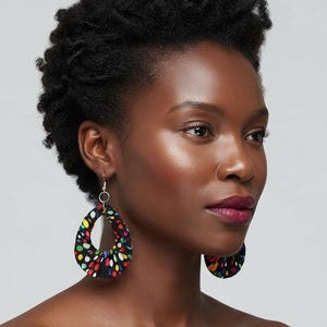 May include: A pair of teardrop-shaped fabric earrings featuring a black base with a vibrant multicolored polka dot pattern. The earrings are suspended from small silver-toned metal hoops and display a gathered, pleated texture throughout the fabric.