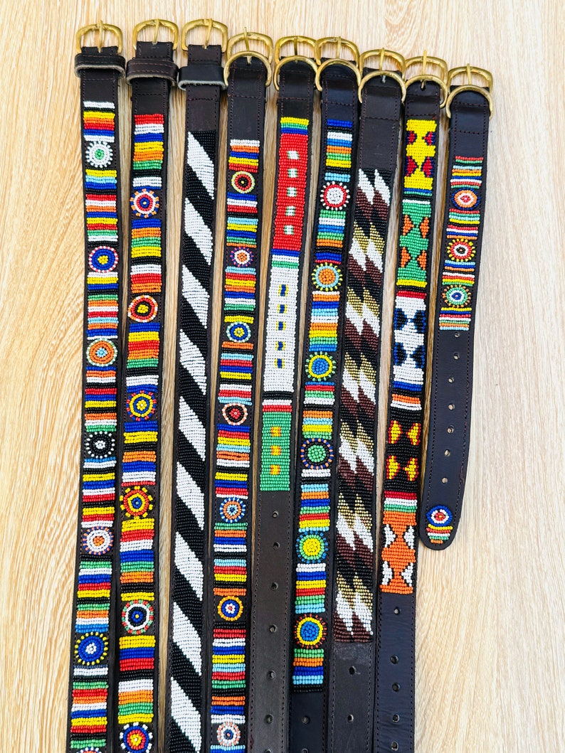 May include: Ten leather belts with colorful beaded designs. The belts are all black leather with brass buckles. The beaded designs are different on each belt and feature a variety of colors, including red, blue, green, yellow, and white.