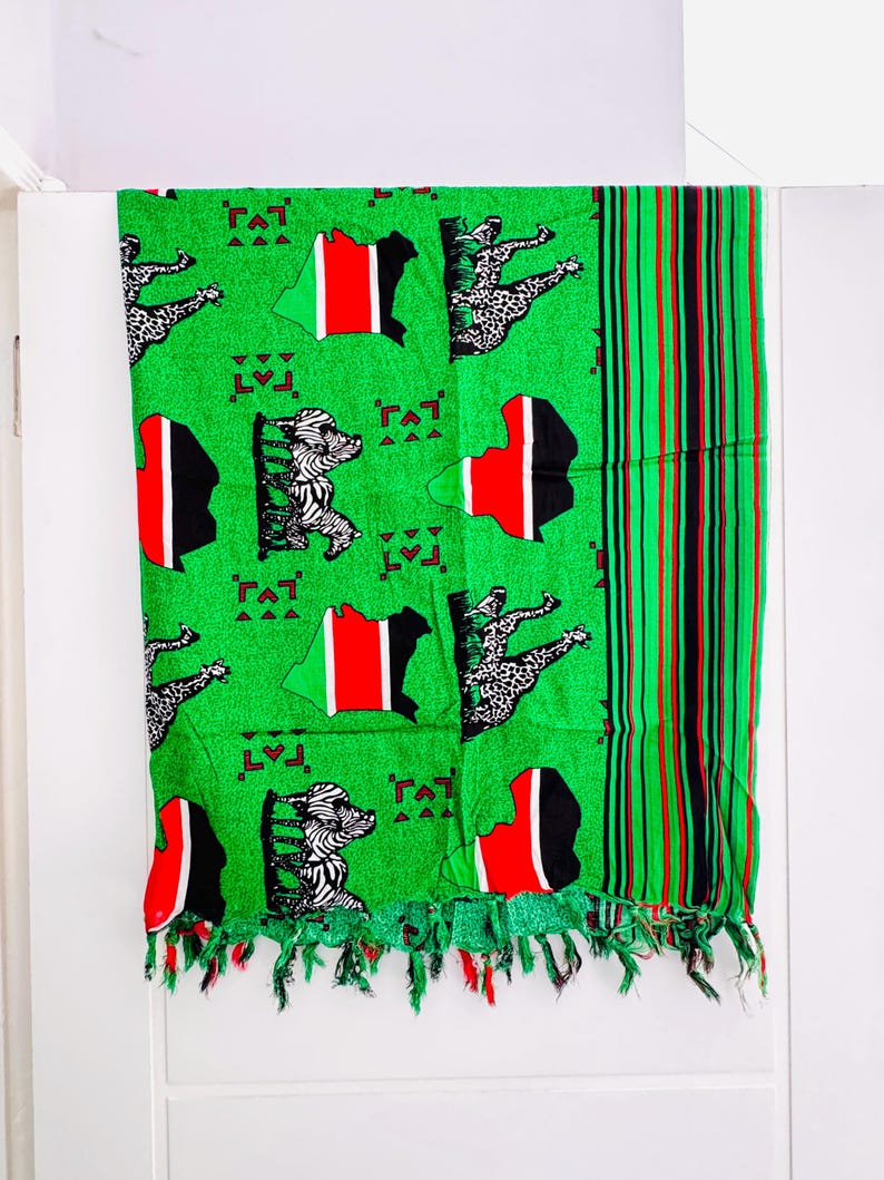 Pu&ograve; includere: Tessuto verde con un motivo che raffigura la mappa del Kenya in rosso, nero e bianco, insieme a figure di zebra e leopardo. Ha un bordo con frange e un bordo a righe rosse, nere e verdi.