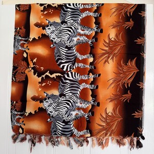 Pu&ograve; includere: Sciarpa rettangolare con stampa zebrata. La sciarpa presenta un motivo ripetuto di zebre in bianco e nero su uno sfondo arancione e marrone. I bordi sono rifiniti con nappe.