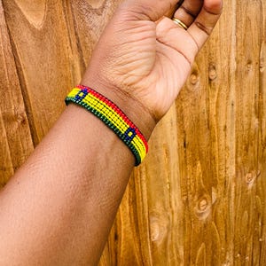 May include: A beaded bracelet featuring horizontal rows of small, uniform beads in vibrant red, yellow, green, and blue colors. The design consists of a repeating pattern of these four colors arranged in a narrow, flat, and flexible band structure.