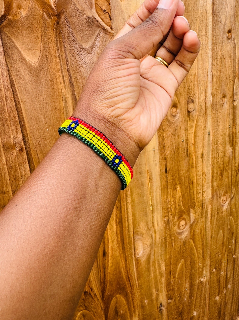 May include: A beaded bracelet featuring horizontal rows of small, uniform beads in vibrant red, yellow, green, and blue colors. The design consists of a repeating pattern of these four colors arranged in a narrow, flat, and flexible band structure.