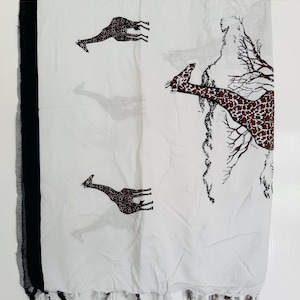 Pu&ograve; includere: Sciarpa bianca con bordo e frange nere. La sciarpa presenta un motivo ripetuto di giraffe marroni con un design maculato. &Egrave; presente anche un disegno simile a un albero sulla sciarpa.