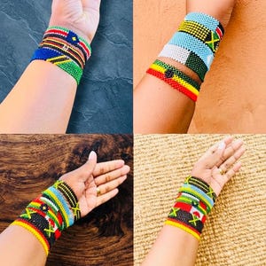 May include: A collection of four sets of multi-coloured beaded bracelets featuring intricate geometric patterns and vibrant flag-inspired designs. Each bracelet is crafted from small, uniform glass beads arranged in horizontal rows, showcasing various colour combinations including red, yellow, green, black, blue, and white.