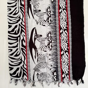 Pu&ograve; includere: Sciarpa bianca e nera con un motivo zebrato. La sciarpa presenta un pannello centrale con illustrazioni di zebre, bordato da motivi decorativi e una striscia rossa. Le nappe adornano il bordo inferiore.