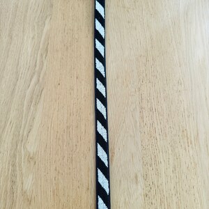 May include: A black leather belt with a white and black geometric pattern. The belt has a gold buckle.