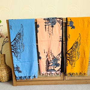 Pu&ograve; includere: Tre sciarpe colorate con un motivo a zebra e albero. Le sciarpe sono blu, pesca e gialle, ognuna con un motivo diverso. Le sciarpe hanno una frangia sul fondo e sono esposte su una mensola di legno.