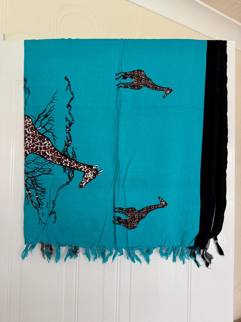 Pu&ograve; includere: Una sciarpa turchese con stampa di giraffe e frange nere. La sciarpa presenta giraffe marroni con un motivo a pois e un disegno ad albero. La sciarpa &egrave; realizzata in un materiale leggero.