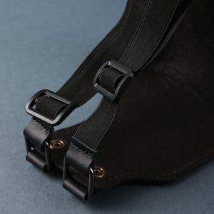 Peut inclure: Gros plan sur un sac en toile noir avec des bretelles r&eacute;glables. Les bretelles sont munies de boucles noires et sont fix&eacute;es par des rivets m&eacute;talliques.
