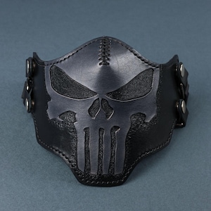 Peut inclure: Masque facial en cuir noir avec un motif de cr&acirc;ne cousu. Le masque est dot&eacute; de sangles r&eacute;glables avec des boucles m&eacute;talliques.