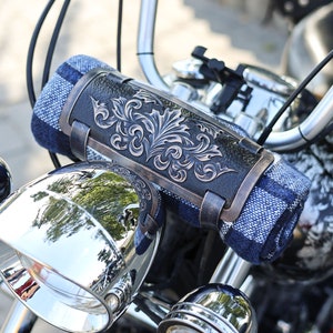Op de afbeelding: Een blauwe en witte geruite motorfiets stuurband met een decoratieve metalen sluiting met een sierlijk bloemmotief.