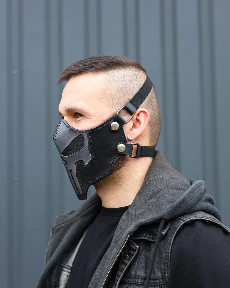 Peut inclure: Un masque facial en cuir noir avec un motif de cr&acirc;ne gris. Le masque est dot&eacute; de sangles r&eacute;glables et est port&eacute; par une personne.