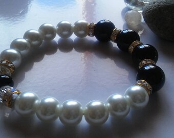 May include: A white and black beaded bracelet with gold accents and clear rhinestones. The bracelet is made of faux pearls and black beads.