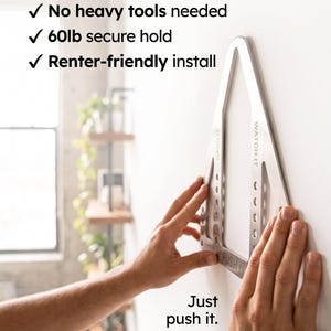 May include: A silver triangular TV mount with the text 'PUSH IT', 'HANG IT', and 'WATCH IT' printed on the frame. The text above reads: 'The only TV mount made for: Zero drywall damage, No heavy tools needed, 60lb secure hold, Renter-friendly install'.