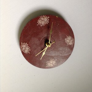 Puede incluir: Un reloj rojo con diseños florales blancos en la esfera. Las manecillas del reloj son doradas.