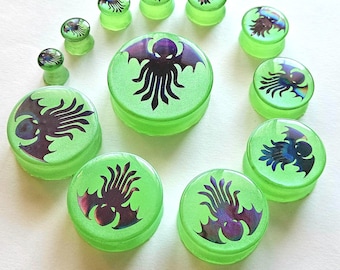 May include: Set of green iridescent ear gauges with a black Cthulhu design. The gauges are various sizes and are made of acrylic.
