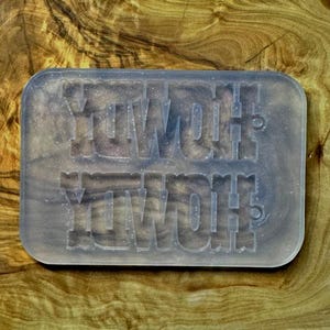 May include: A rectangular, translucent soap bar with the word "YOWOH" imprinted twice. The soap has a marbled appearance and sits on a wooden surface. The soap's rounded corners and the wood grain create a natural aesthetic.