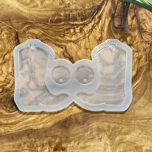 May include: Clear silicone mold for making resin earrings in the shape of cowboy boots. The mold has two boot shapes and two small circles for earring posts.