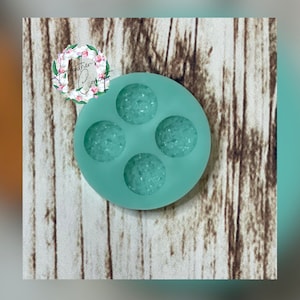 May include: A light green silicone mold with four round cavities. The cavities have a textured surface that resembles small pebbles.