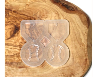 May include: Clear plastic mold for making baseball-themed earrings. The mold has two baseballs and two medallions with holes for earring posts.