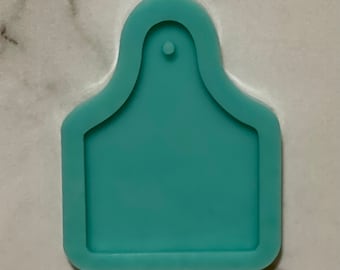 May include: A light blue silicone mould shaped like a cow tag with a hole at the top for hanging.