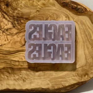 May include: A clear silicone mold with the word "EAGLES" written twice in a glittery, light purple color.