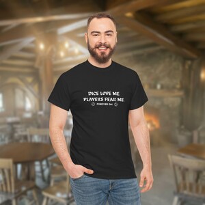 May include: Black t-shirt with white text that reads "DICE LOVE ME. PLAYERS FEAR ME. FOREVER DM" and two dice symbols. The shirt is worn by a person in a room with a blurred background.