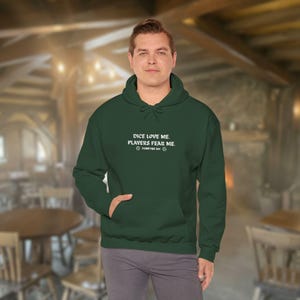 May include: A dark green hoodie with the text "DICE LOVE ME, PLAYERS FEAR ME" in white. The hoodie has a front pocket and a drawstring hood. The text also includes the words "FOREVER DM" and a dice graphic.