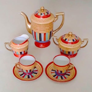 Könnte beinhalten: Ein Vintage-Tee-Set mit einem farbenfrohen geometrischen Design. Das Set enthält eine Teekanne, eine Milchkännchen, eine Zuckerdose und zwei Teetassen mit Untertassen. Die Teile sind mit Streifen in Rot, Orange, Gelb, Grün, Blau und Schwarz verziert.