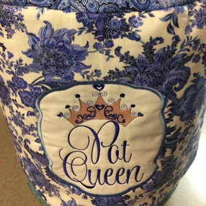 May include: A white and blue floral fabric appliance cover with a gold crown and the embroidered text "Pat Queen".